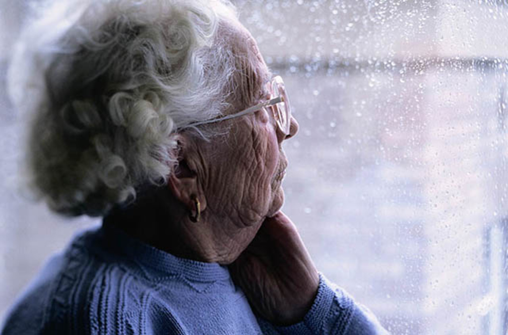 Elderly woman looking out window at rain