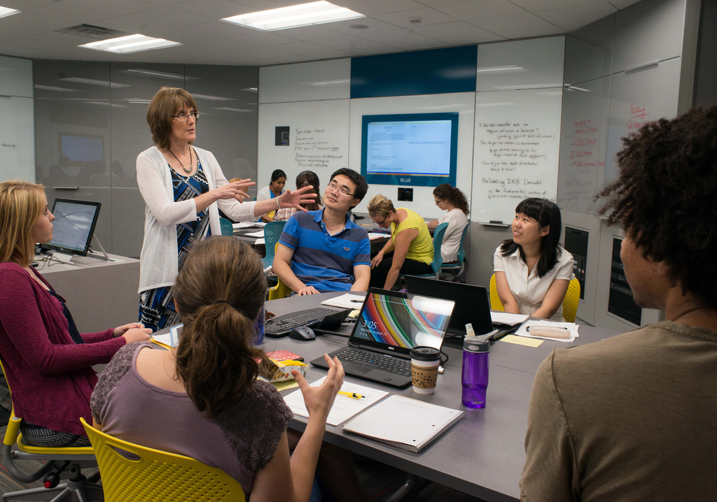 Professor Kathy Schuh leading discussion with a pod of students in N105 classroom.