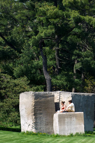 two students sitting on the Utterback sculpture, pinetrees in the background