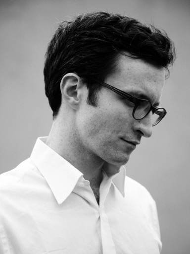 A photo of a young man wearing black glasses and a white shirt