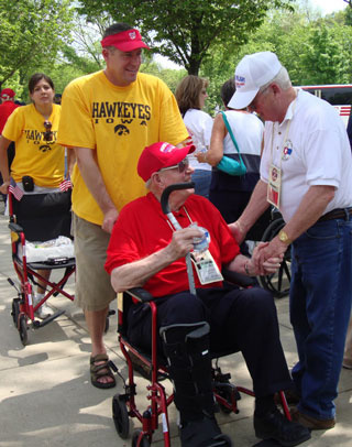 Man in Iowa Hawkeyes t-shirt pushes a veteran in a wheelchair.