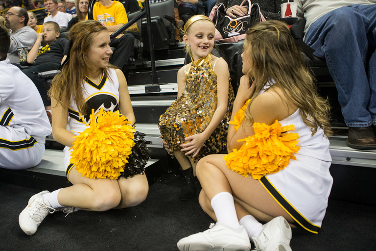 Cheerleaders talk to a little girl in a gold sequined outfit.