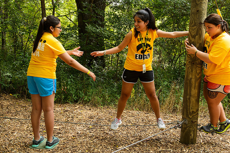 Three students hold hands while working through an obstacle course as part of a team building activity in The Iowa Edge Program.