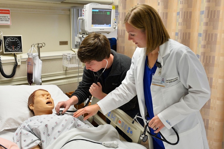 People listening with stethoscope to a nursing simulator's chest.