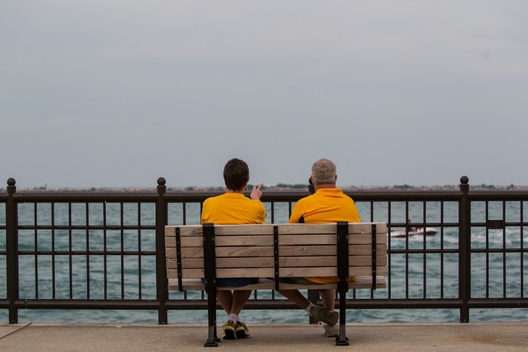 A couple in yellow t-shirts sit on a bench and look out over a body of water.