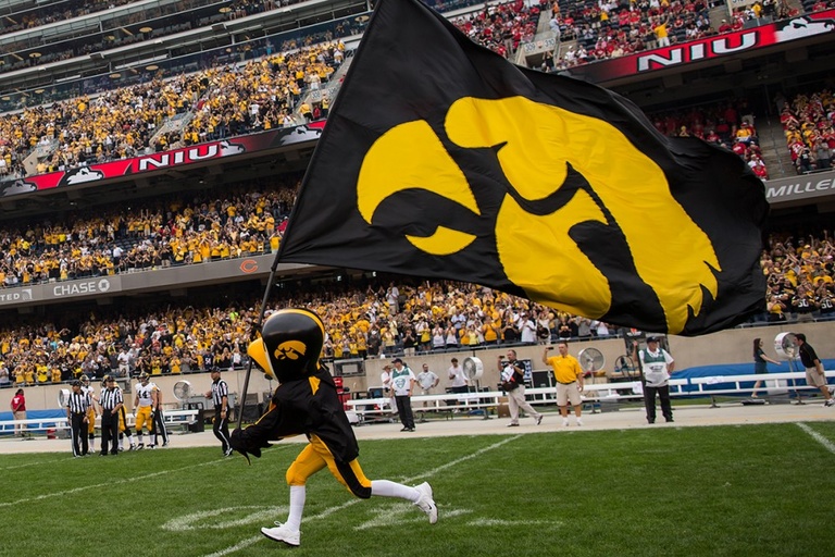 Iowa mascot Herky runs onto a football field flying a Tigerhawk flag.