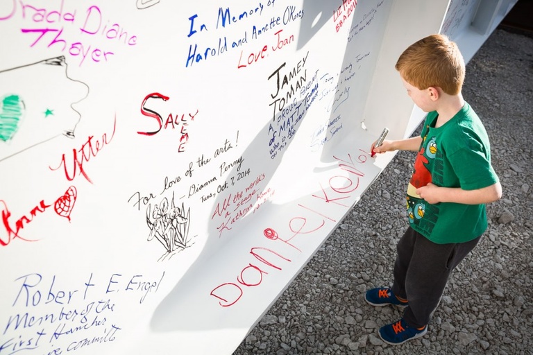 A young boy writes his name on a beam.