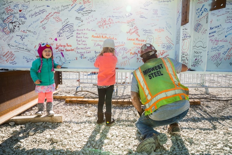 Two young girls and one construction worker write on a steel beam