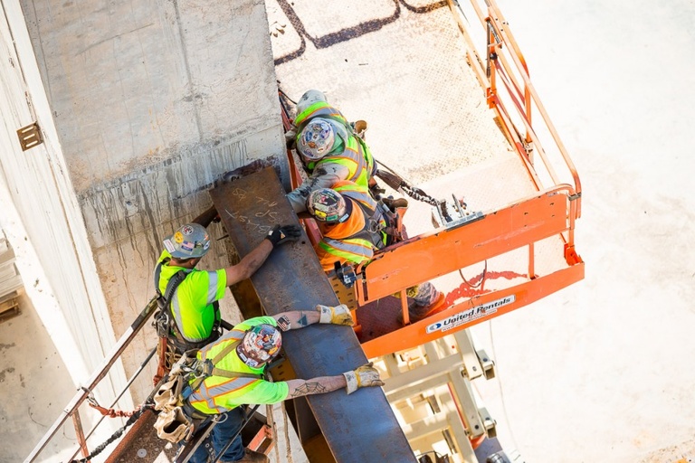 Four construction workers surrounding a large steel beam.