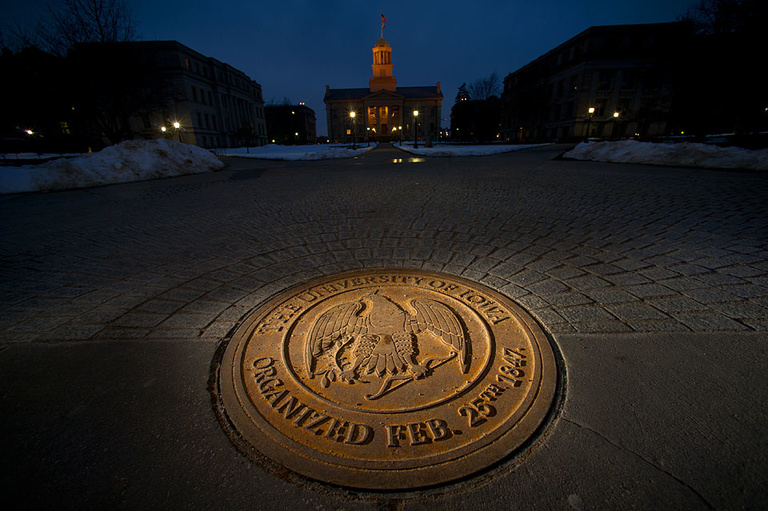 A utility cover with the University of Iowa seal, Old Capitol in the background. 