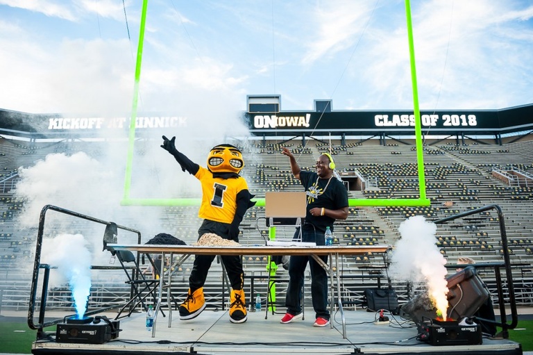 Herky and DJ on stage with Kinnick Stadium goalposts in the background.