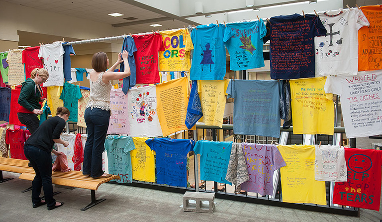 People hang shirts while setting up the Clothesline Project.