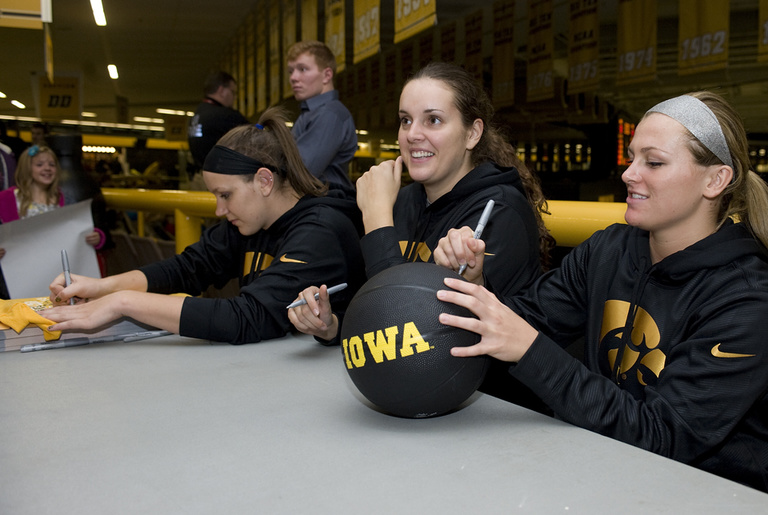 Three women autographing a basketball.