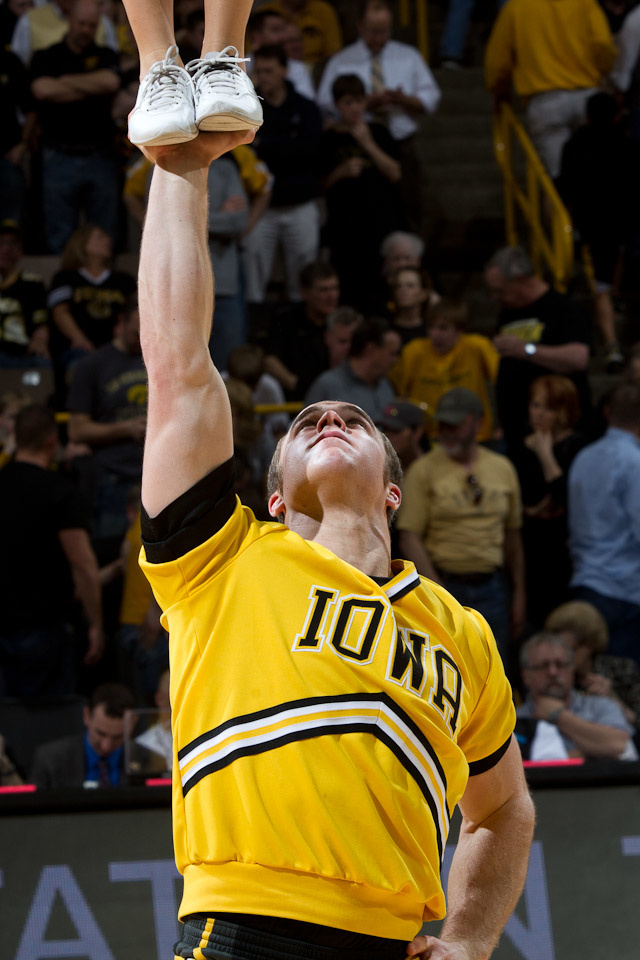 An Iowa male cheerleader holds another cheerleader above his head, you can see only her feet in the upper left corner.