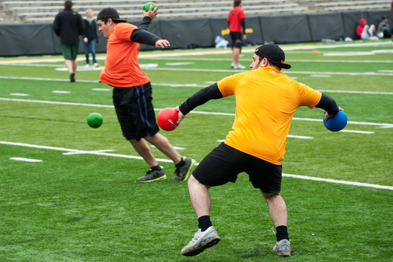 a dodgeball player throws a ball while another player jumps to avoid being hit by a ball