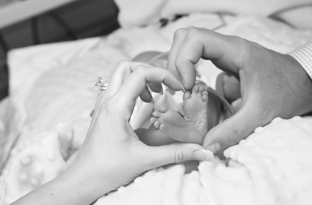 a man's hand and a woman's hand forming the shape of a heart around their child's feet