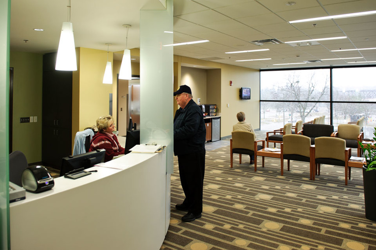 A man speaks to a receptionist in a College of Dentistry clinic waiting room.