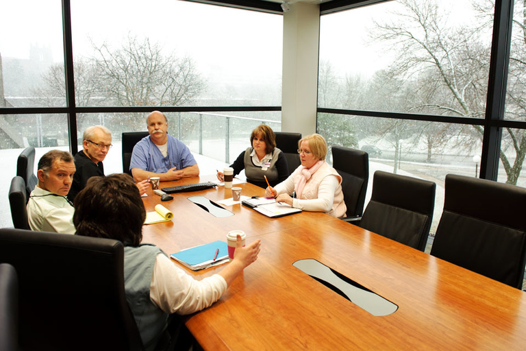 Staff members gather at a large conference table in a glass-walled meeting room.
