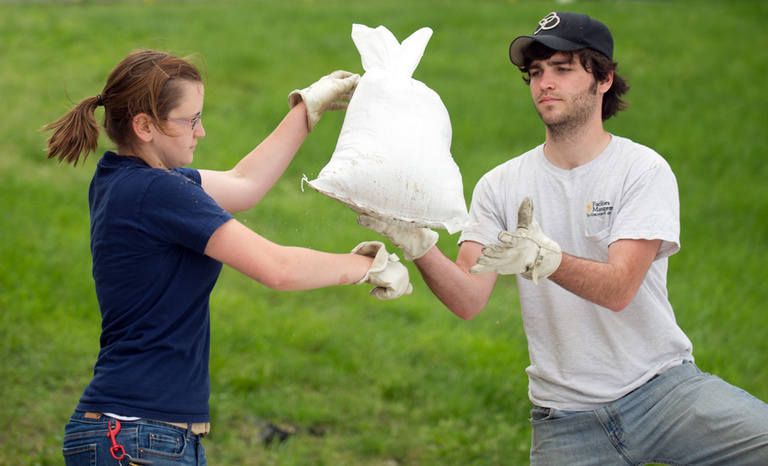 A woman passes a sandbag to a man who are both helping prepare for potential flooding on the Ui campus.