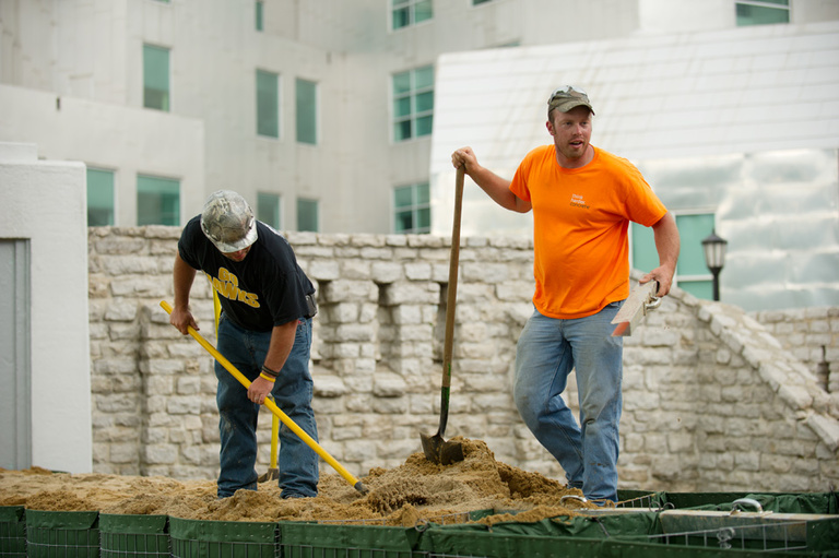 Workers shovel sand into HESCO barriers.