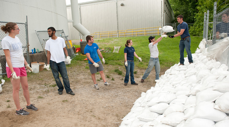 A group forms a line, working together to pass sandbags on campus.