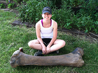 A woman sits with a huge mammoth bone.