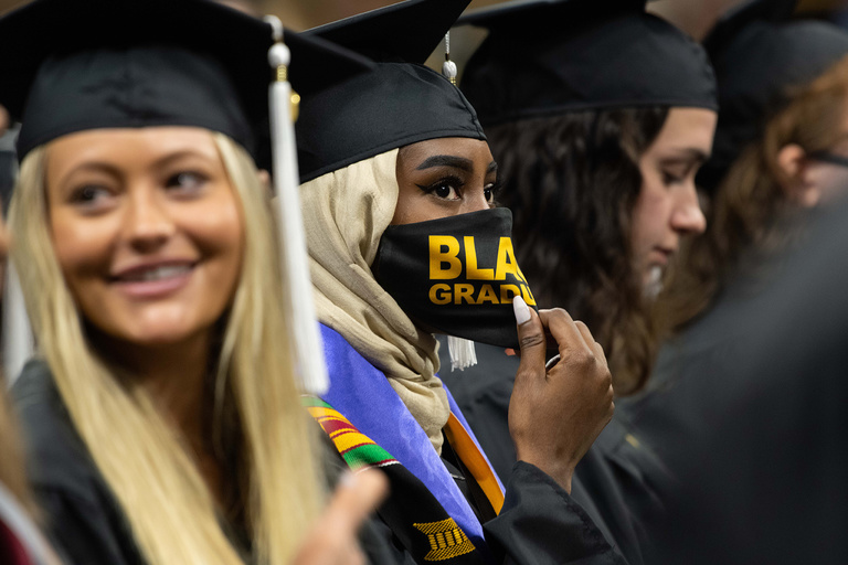 A graduate adjusts their mask during the College of Liberal Arts and Sciences commencement ceremony. Photo by Tim Schoon.