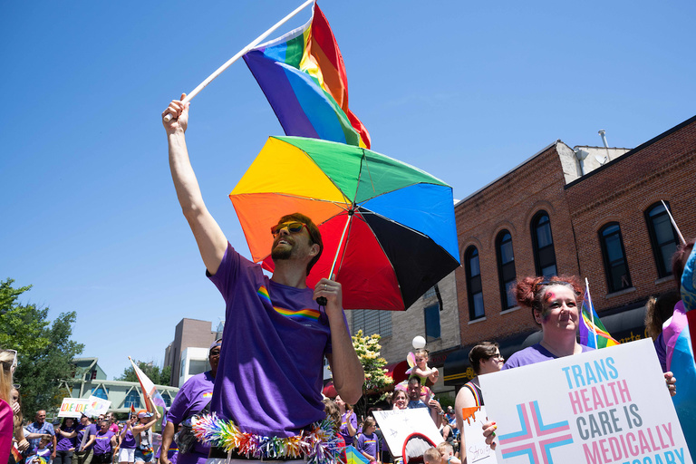 Underneath a Pride flag and Pride umbrella, a parade attendee celebrates the day.