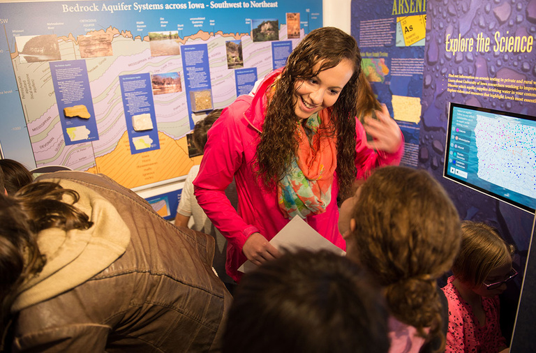 A UI science education students talks to students near a display about Iowa's underground water supply.