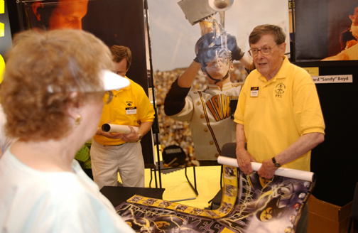 Former President Willard “Sandy” Boyd rolls up posters of Iowa sports teams and hands them out to fans at the Iowa State Fair in 2002.