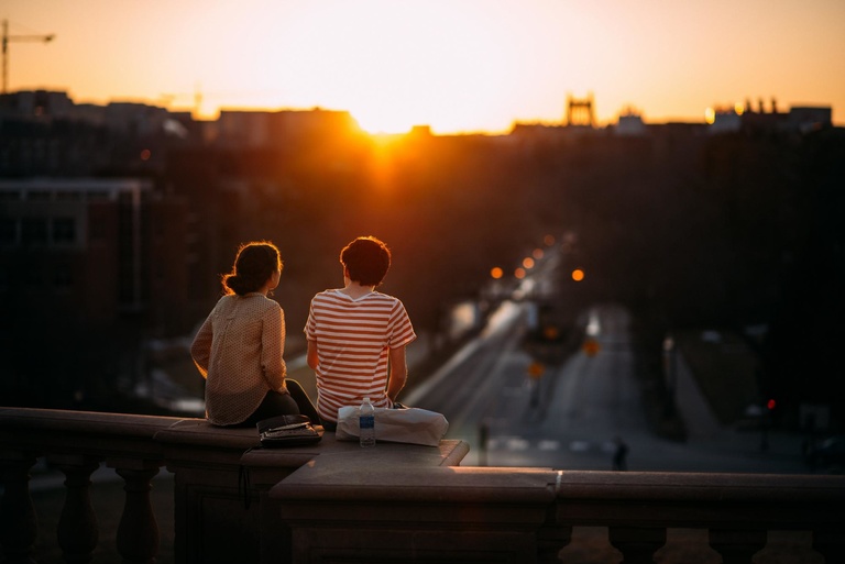 students sitting on Pentacrest railing, overlooking west campus at sunset