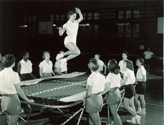 woman jumping on trampoline as other women stand around the trampoline
