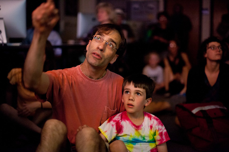 A man and his son sit on the floor looking up.