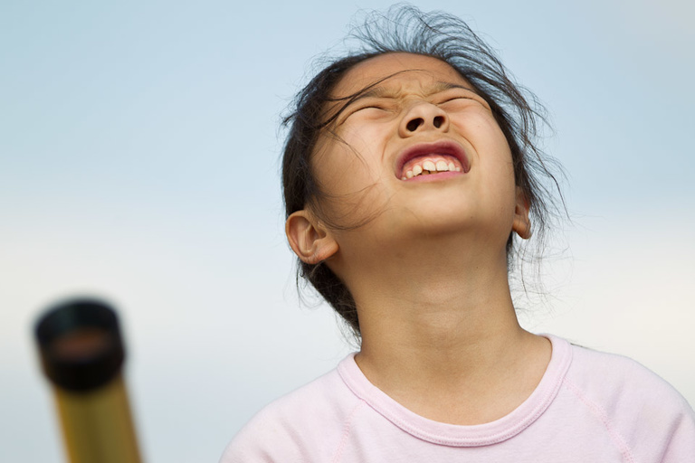 A young girl squints looking into the sky.