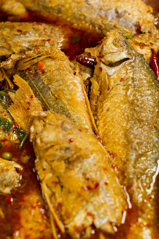 Cooked fish with their heads and scales intact lie in a serving dish with sauce and spices.