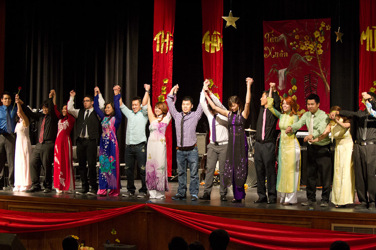 A line of young men and women all with their hands in the air on stage ready to bow.
