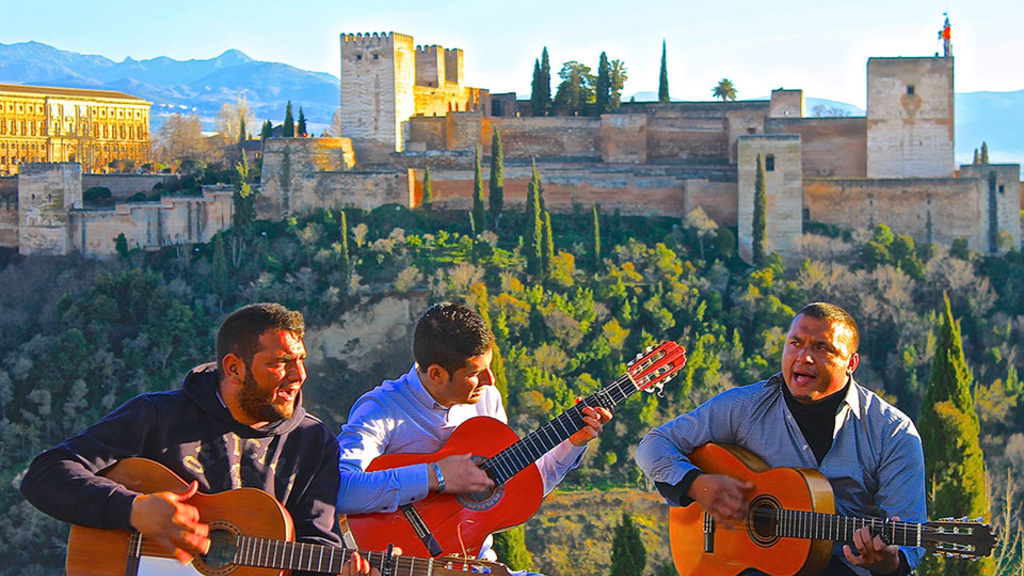 “High up in the mountains with a view of the enchanted Alhambra and snowcapped mountains, a trio of Spanish men sit and play traditional Spanish music with their guitars as people stare out into the endless beauty of Granada.” This photo, "Musica en l