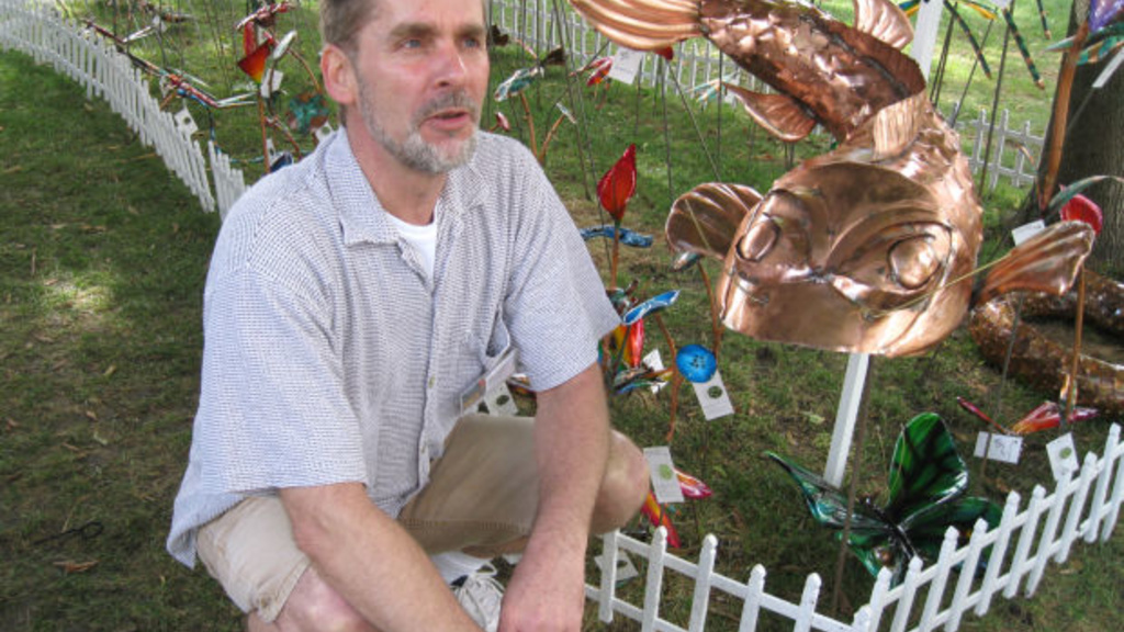 UI alumnus Robert Sample of Mount Pleasant poses with some of his metal art sculptures at the Clear Lake Art Sail including some copper fish