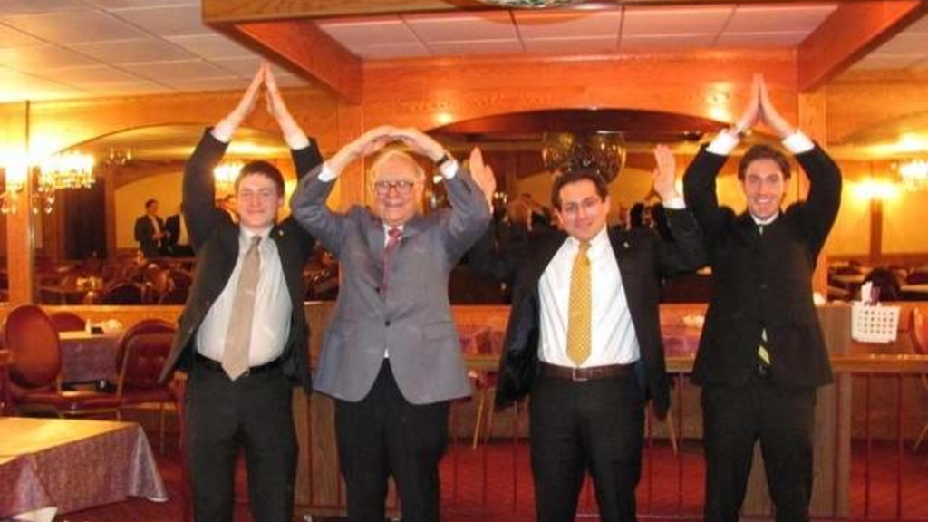 Billionare investor Warren Buffett makes the shape of the letter o with his hands with three other UI business students who are spelling out Iowa with their hands