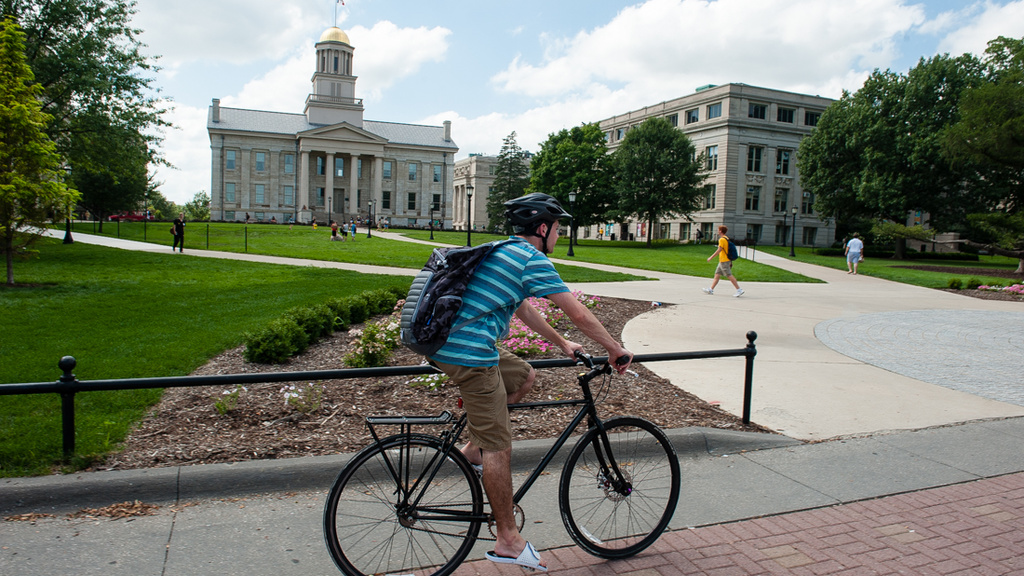 A student rides a bike across campus in front of the UI Pentacrest.