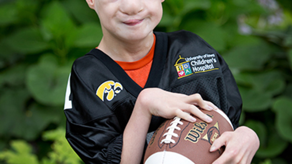 Carson Thomas standing infront of a garden wearing a hawkeye jersey and holding a football.