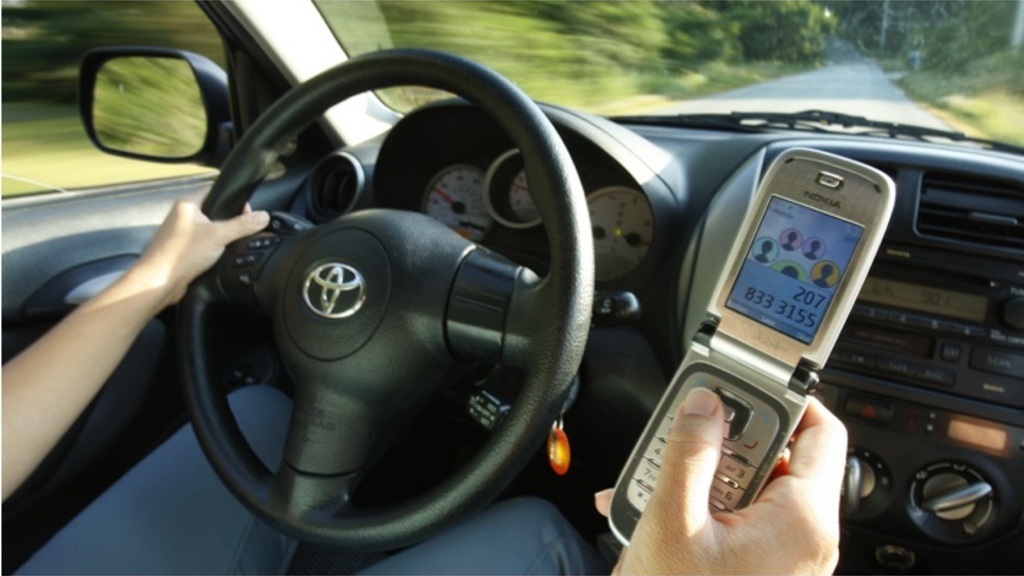 A close up photo of a steering wheel while someone is sending a text message with their right hand while driving