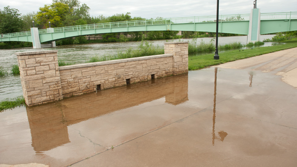 Water spills onto the sidewalk along the Iowa River.