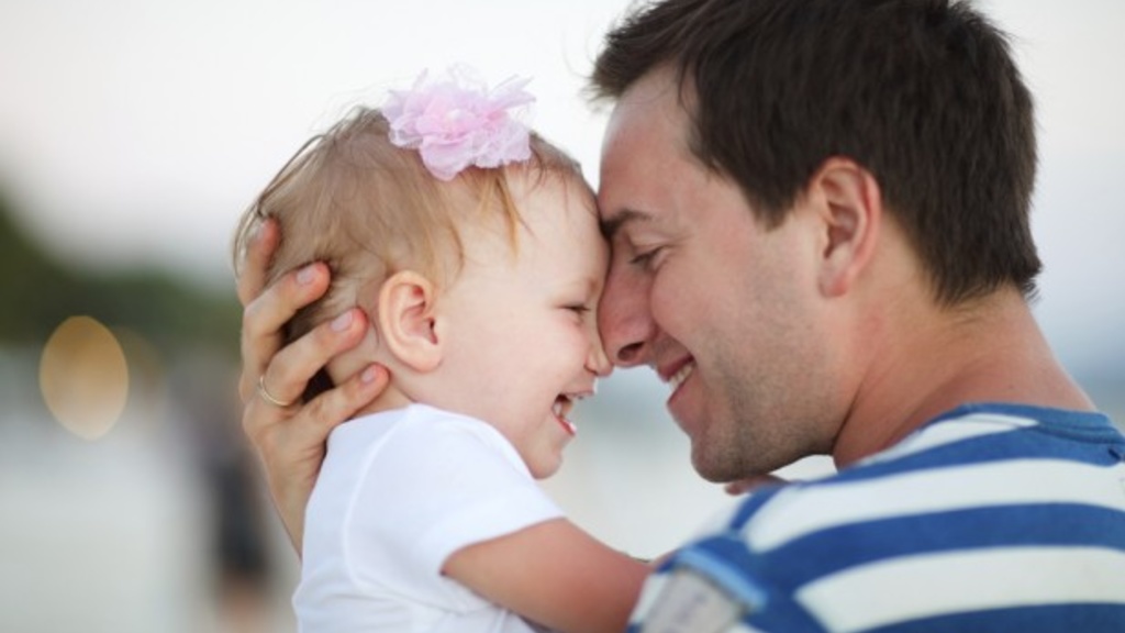 Photo of a Dad with his faced pressed against infant daughter while hugging her