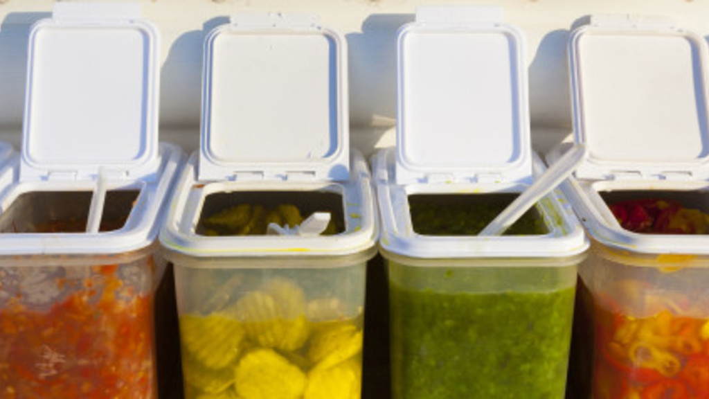 A variety of containers with relishes such as pickles and other hot dog toppings