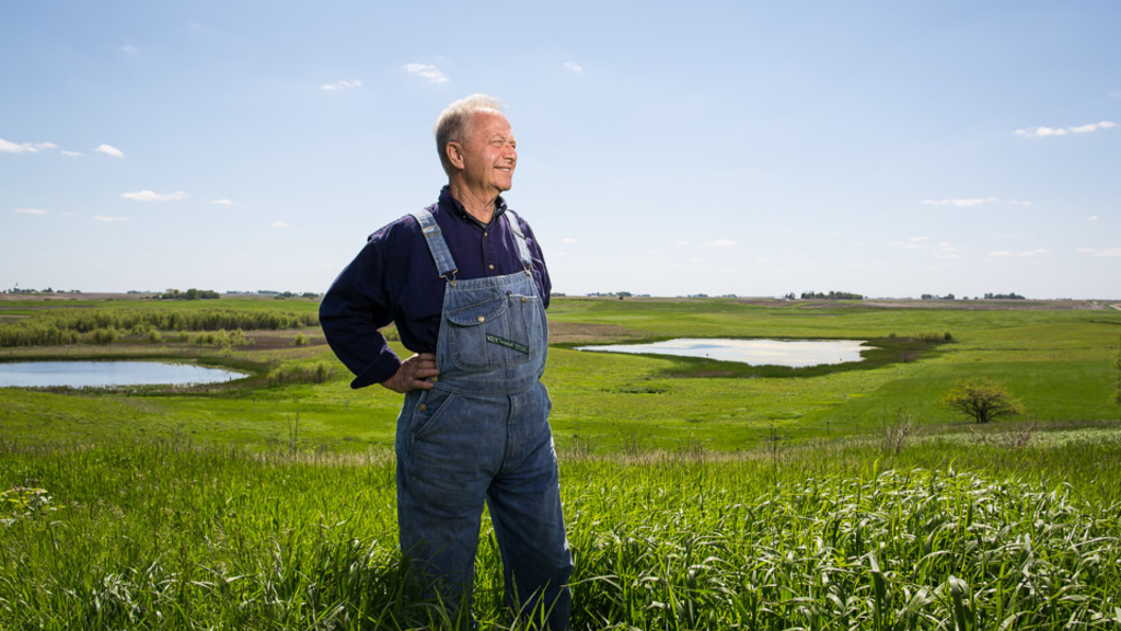 A farmer in bib overalls standing in a field of grass