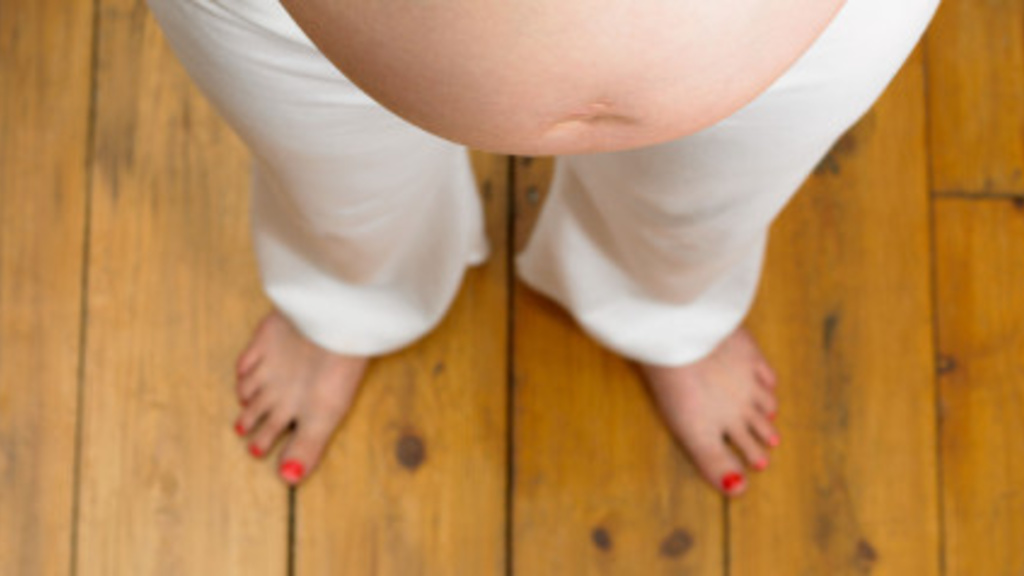 Photo of a pregnant women&#039;s bare stomach from the perspective of looking down at her feet