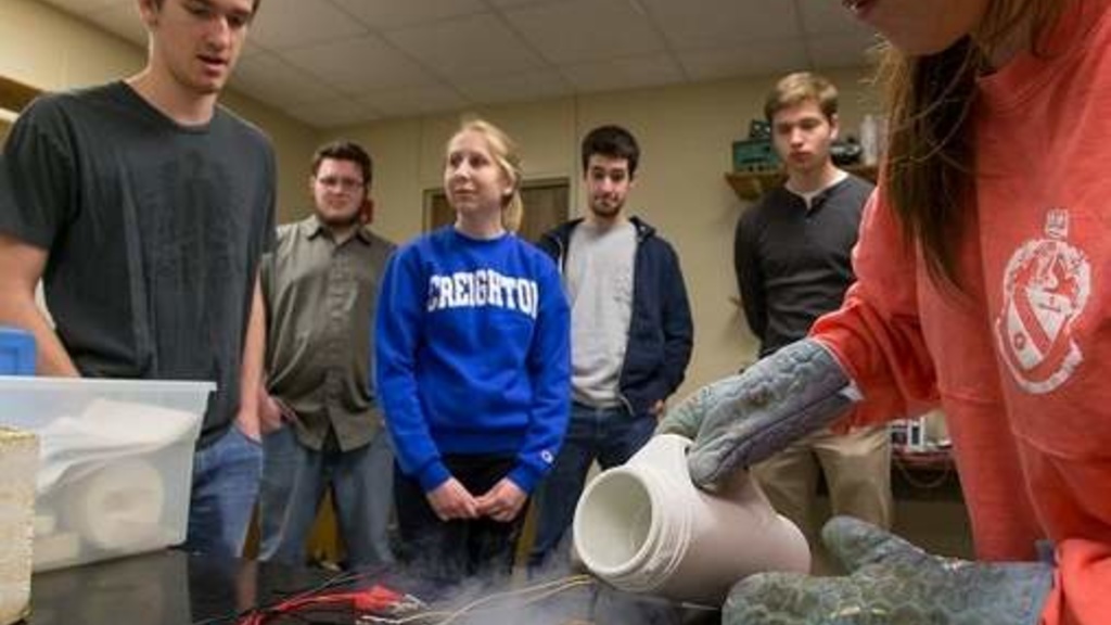 Creighton University student Brianna Baca pours liquid nitrogen as she and her teammates — Chris Rogge, left, and Erin Cheese, at center in blue — lead a demonstration in their materials science class.