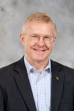 Nick Street, a man with strawberry-blond, short hair wearing round glasses. He's wearing a dark suit jacket and a blue checked shirt. 