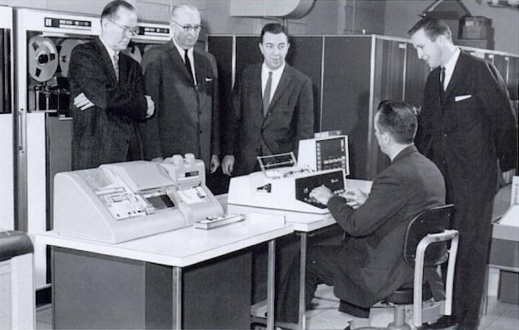 Men in suits standing around an early computer.